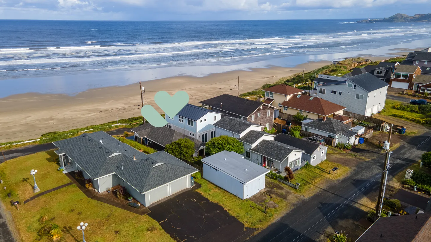 Aerial view of a coastal neighborhood with houses situated along a wide sandy beach and ocean surf.