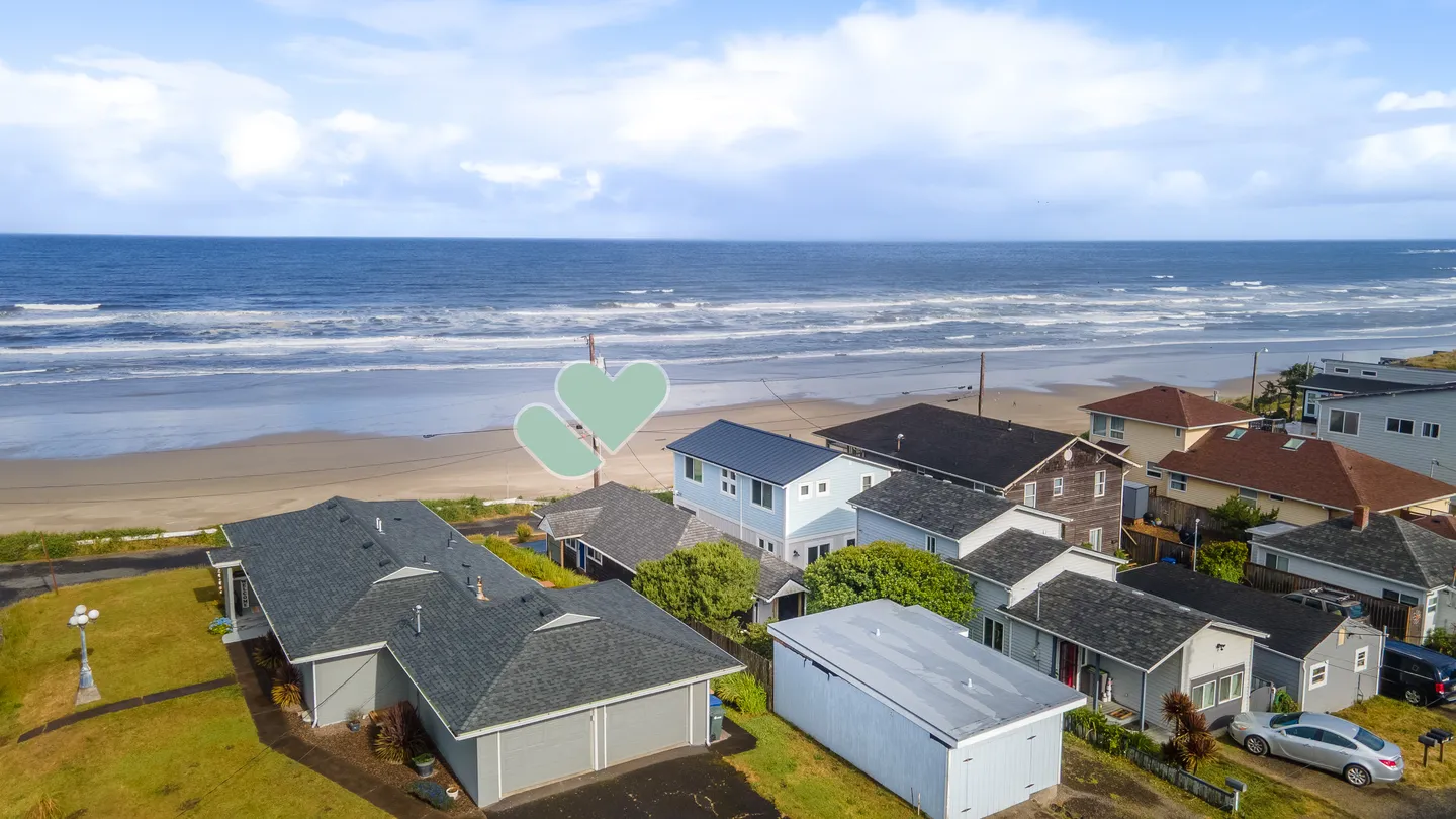 Aerial view of coastal homes situated along an ocean beach with rolling waves under a blue sky.