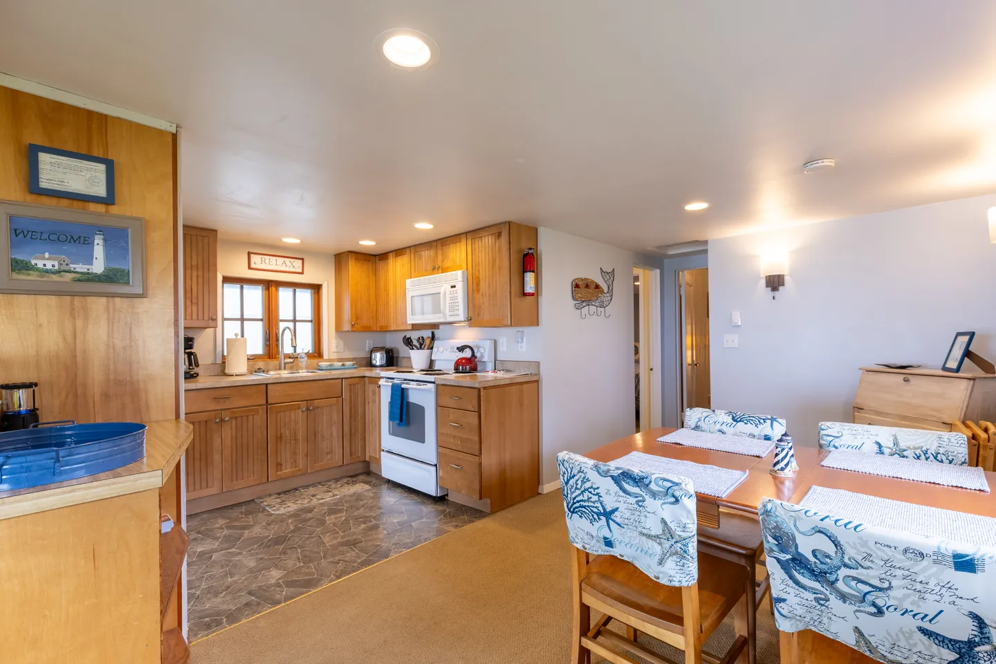 Open-concept dining area and kitchen with wooden cabinets, white appliances, and a dining table with patterned chair slipcovers.