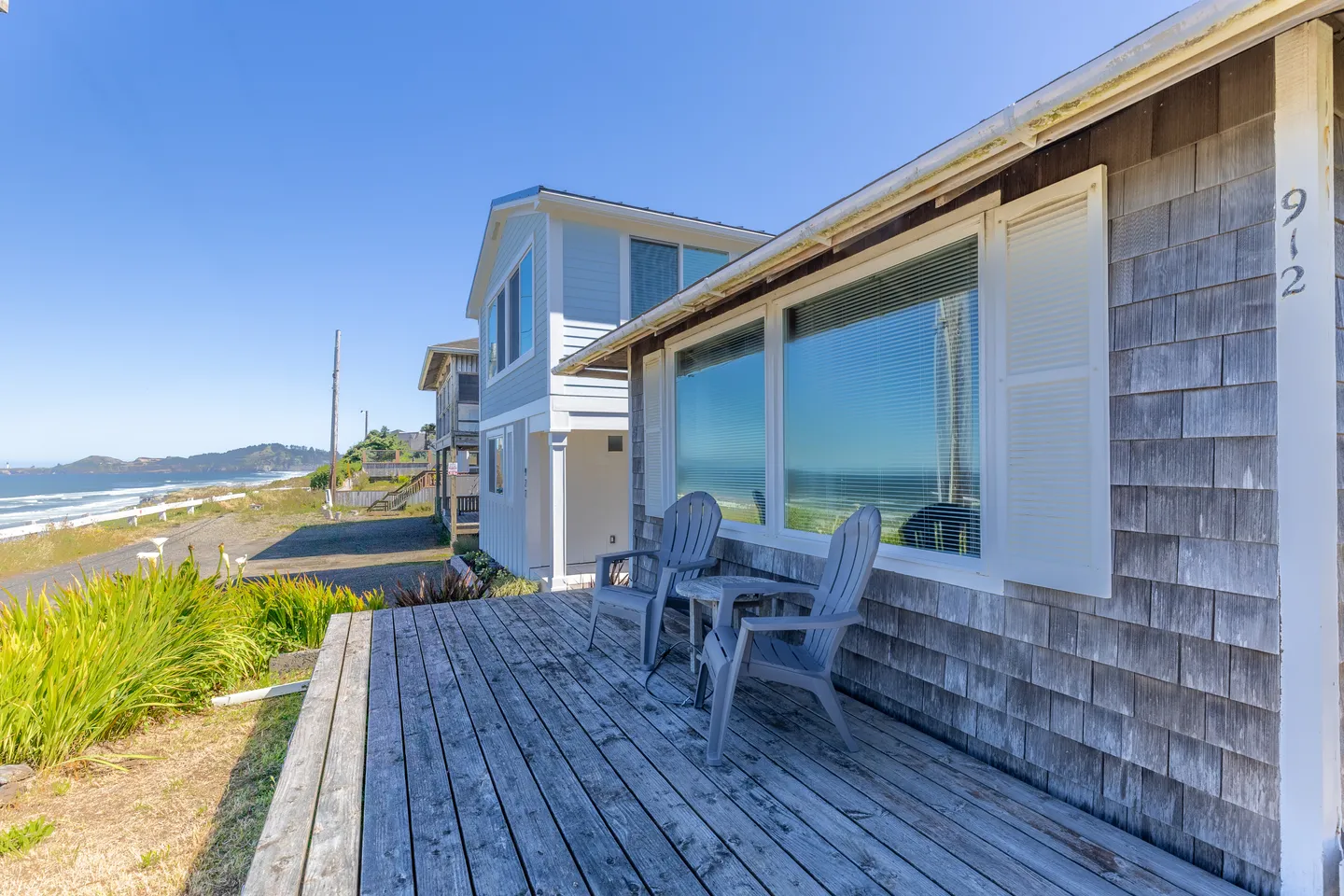 Wooden deck with two outdoor armchairs facing a view of the beach and ocean.