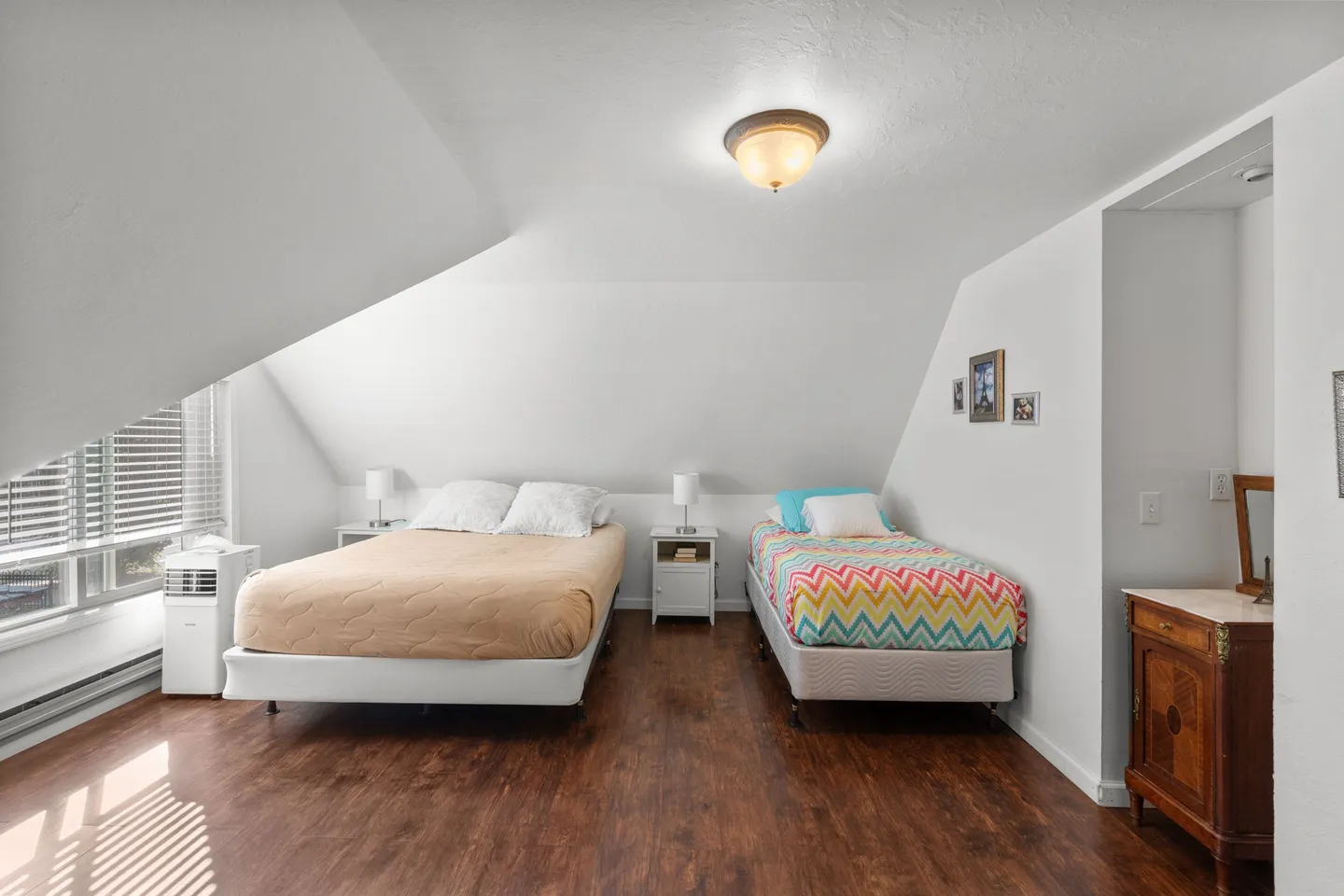 Upstairs bedroom with sloped ceilings, two beds, a window, and dark wood-style floors.