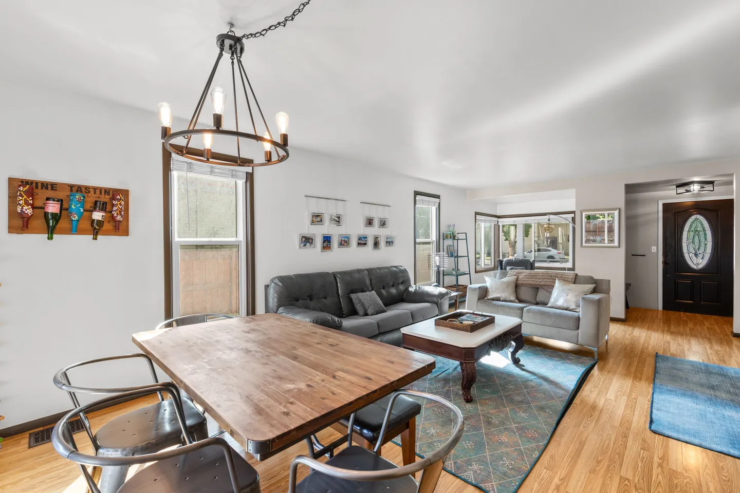 Open living and dining area featuring a wooden dining table with metal chairs, sofas, a coffee table, and an entry door in the background.