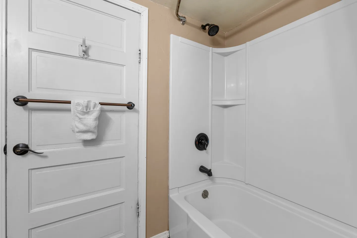 Bathroom showing a white paneled door with a towel rack next to a white bathtub with dark fixtures.