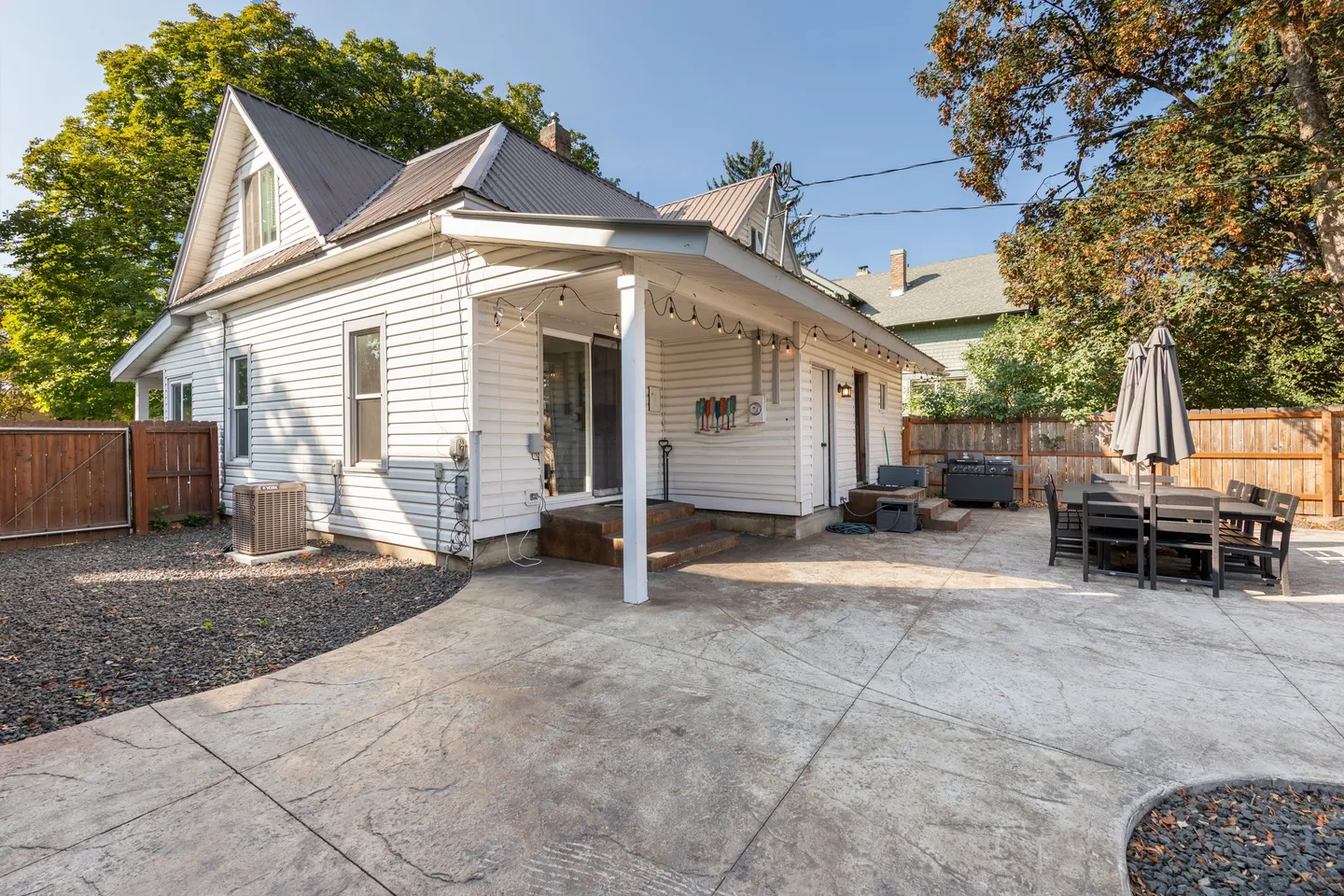 Concrete patio and back exterior of a white siding house with covered porch area and outdoor dining table.