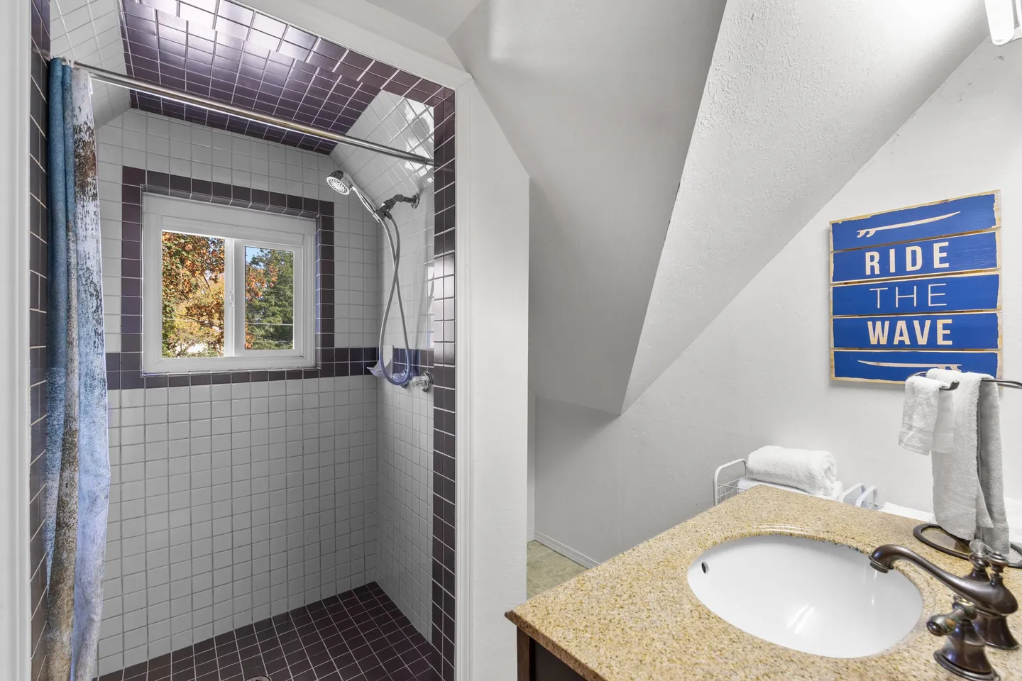 Bathroom with sloped ceiling, vanity with an oval sink, and a tiled walk-in shower with a window.