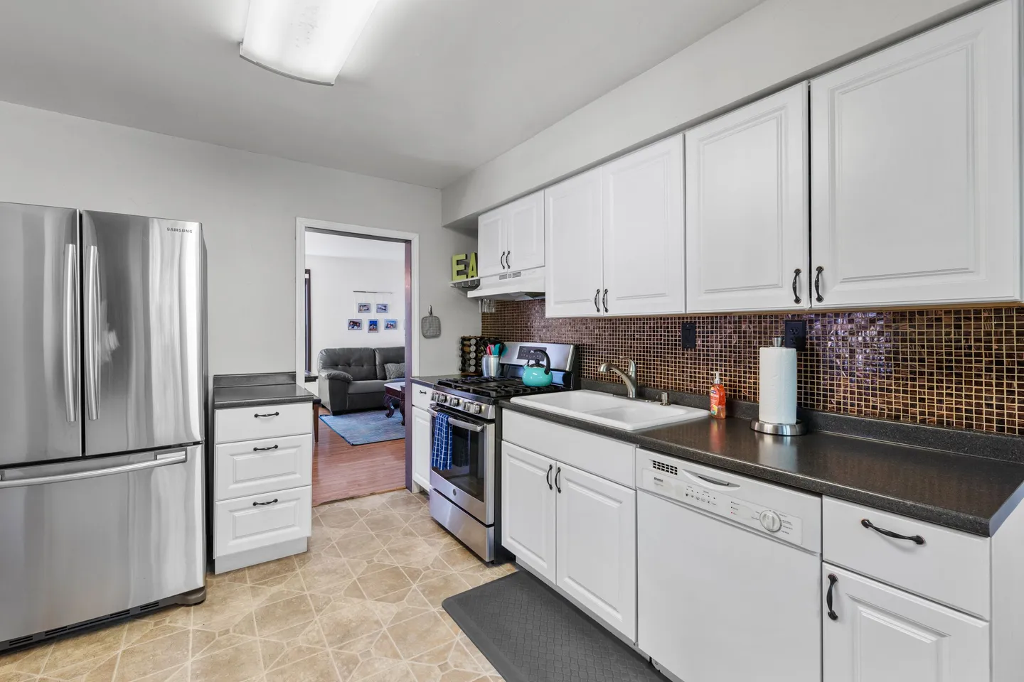 A kitchen with white cabinets, dark countertops, brown mosaic tile backsplash, and stainless steel appliances.
