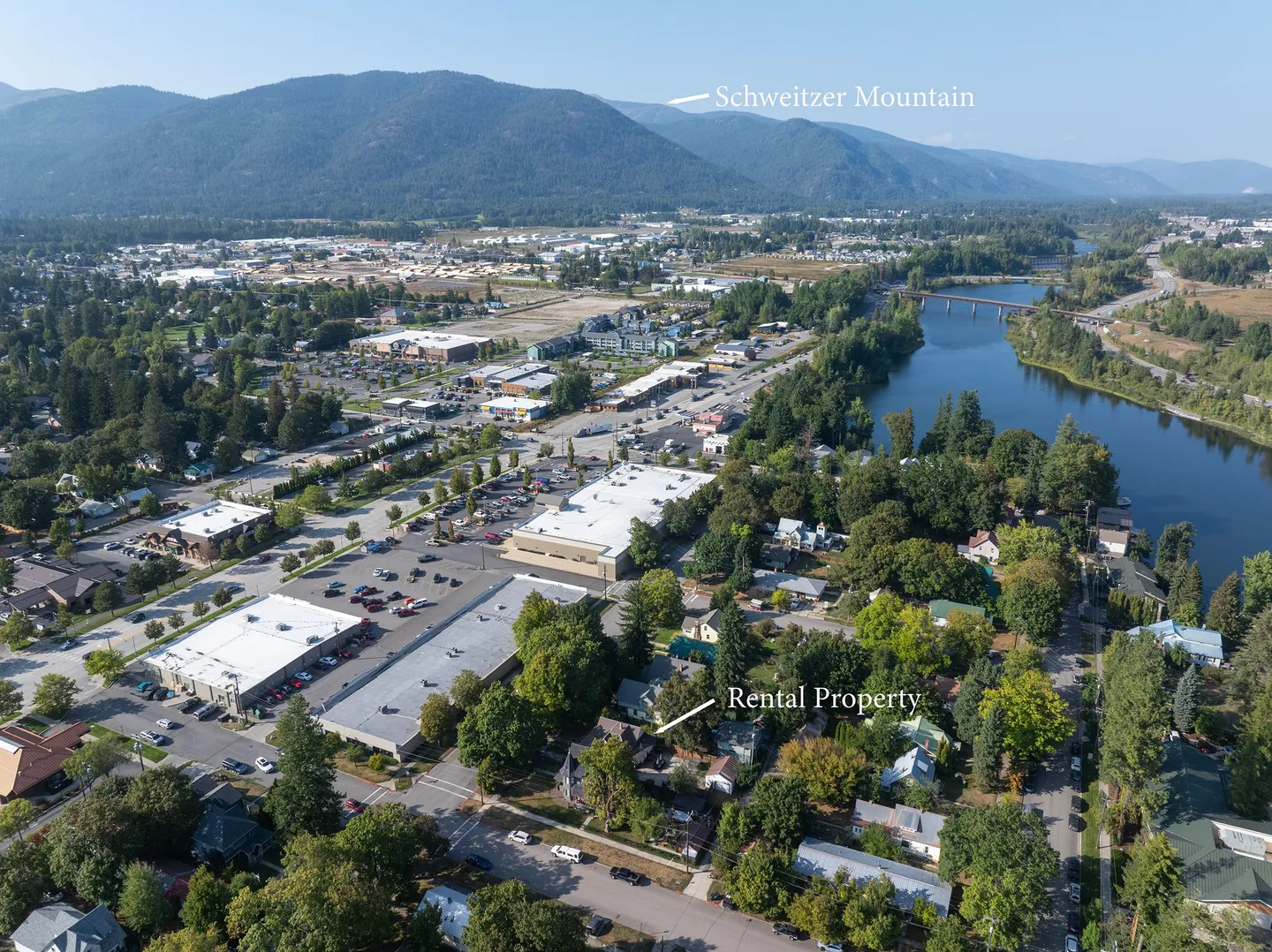 Aerial view showing the rental property neighborhood, adjacent river, town buildings, and distant Schweitzer Mountain.