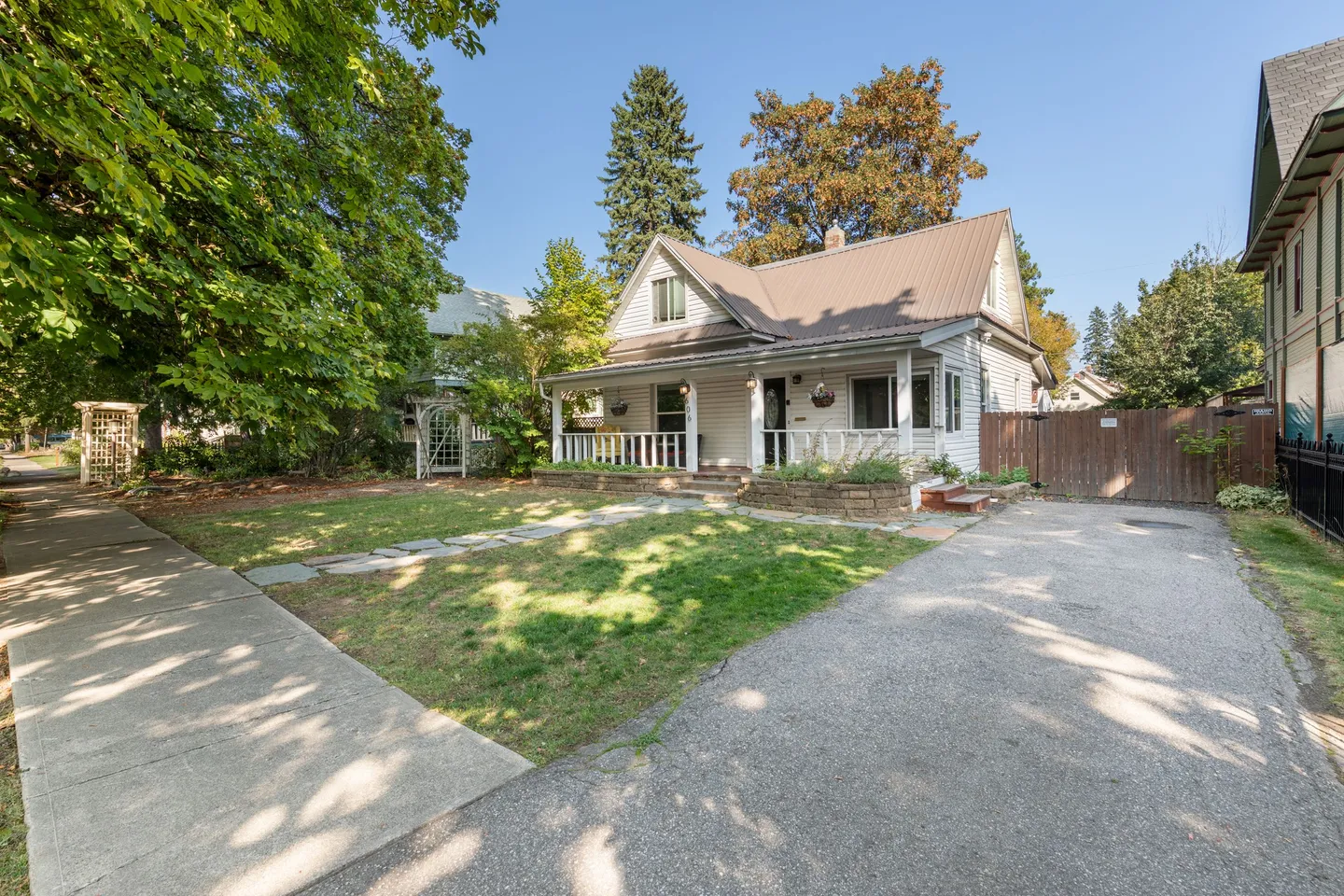 Exterior view of a one-and-a-half-story house with a front porch, lawn, paved driveway, and sidewalk.