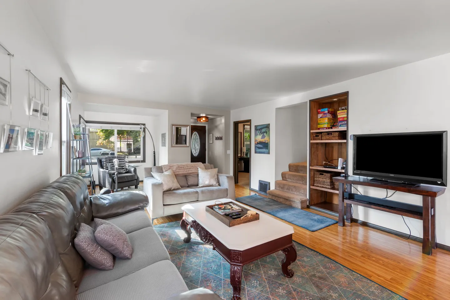 Living room with sofas, a coffee table, a flat-screen TV on a wooden stand, built-in shelving, and stairs leading up.