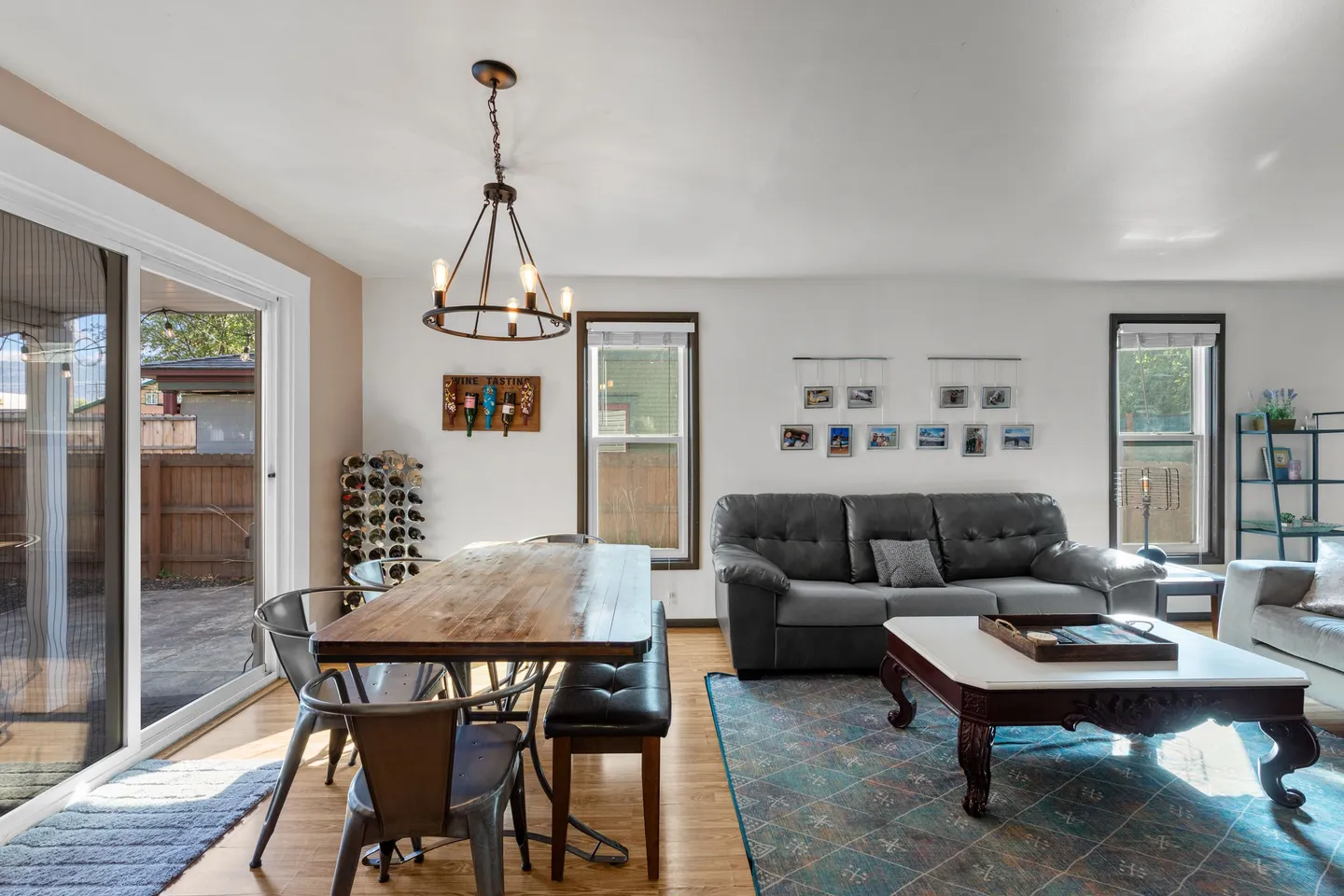 Open concept living and dining area with a wooden table, dark sofa, patterned rug, and sliding glass door leading outside.