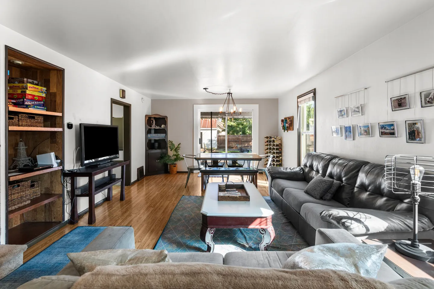 Open-concept living room with leather sofas, TV stand, coffee table, and an adjacent dining area leading to sliding glass doors.