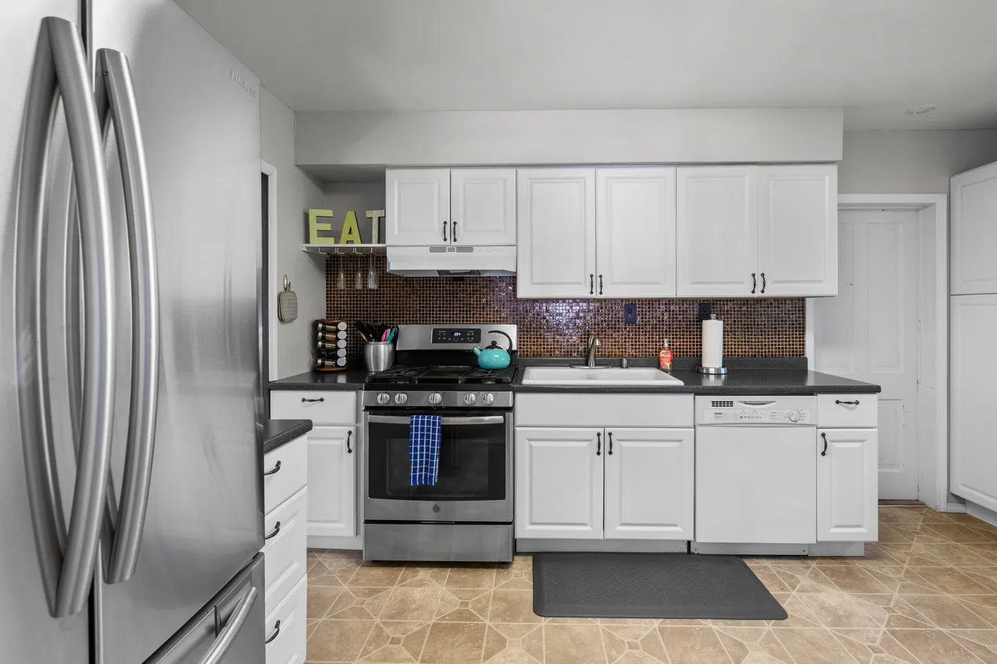 Kitchen with white cabinetry, dark countertops, tile backsplash, and stainless steel appliances.