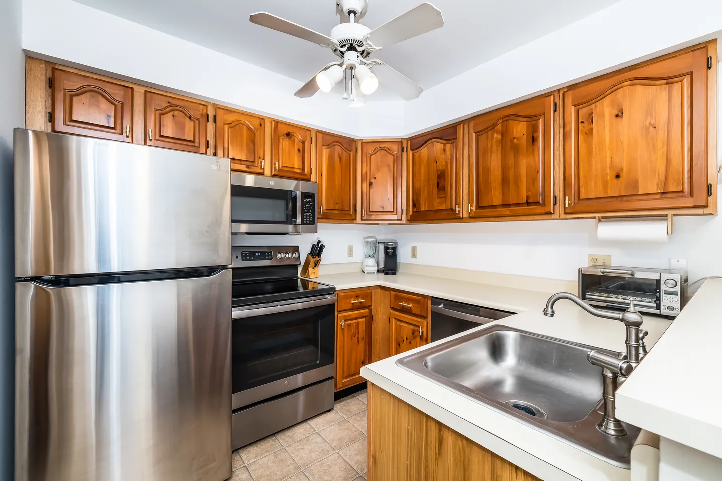 Kitchen with wood cabinetry, stainless steel appliances, laminate countertops, and a ceiling fan.