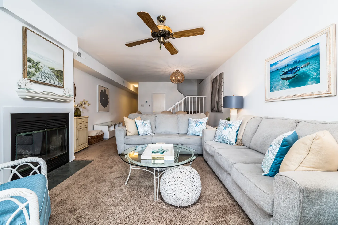 Living room with carpeted floor, light gray sectional sofas, a glass coffee table, a fireplace, and a ceiling fan.
