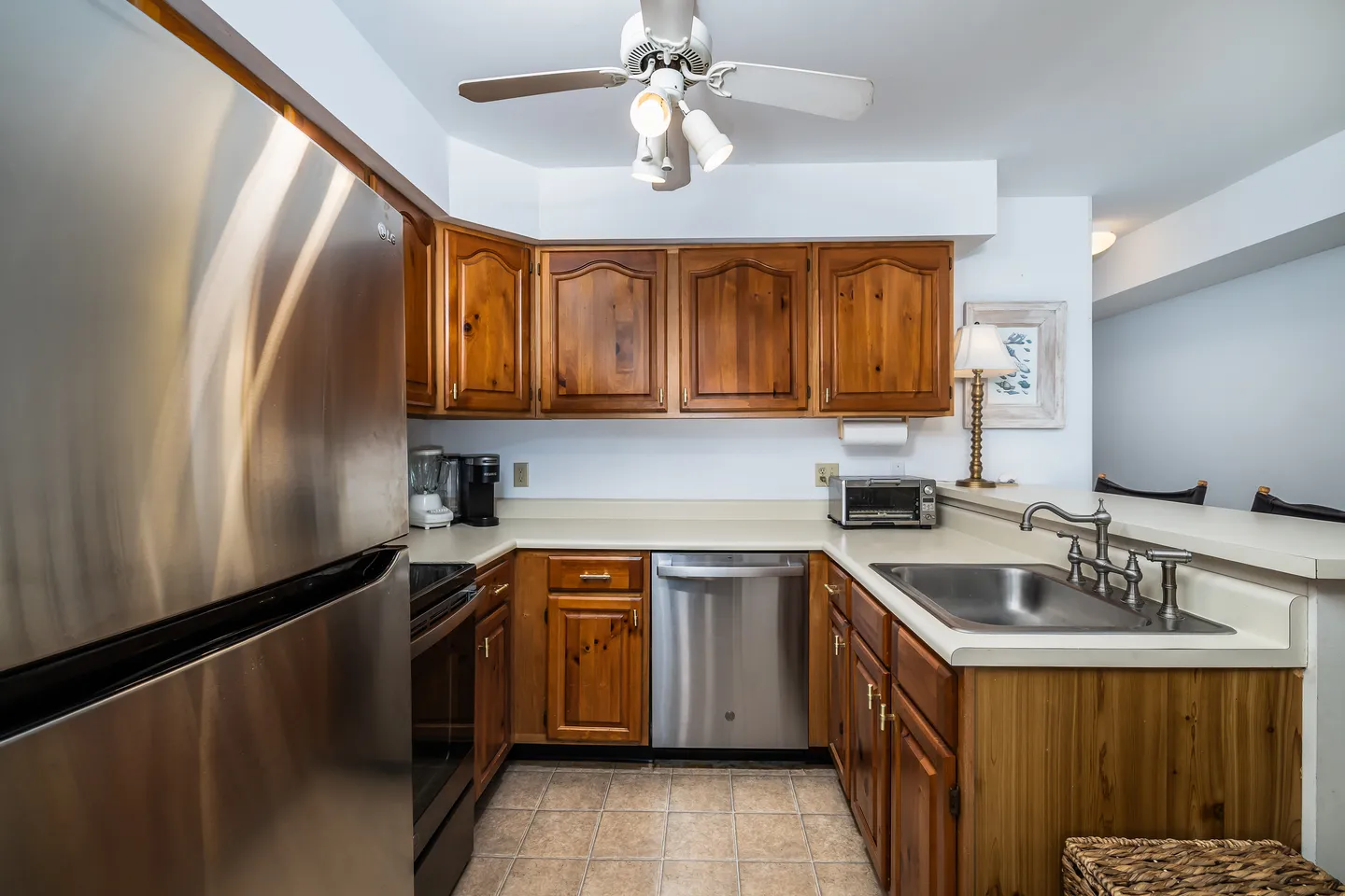Kitchen with wooden cabinetry, laminate countertops, a stainless steel refrigerator, dishwasher, and sink.