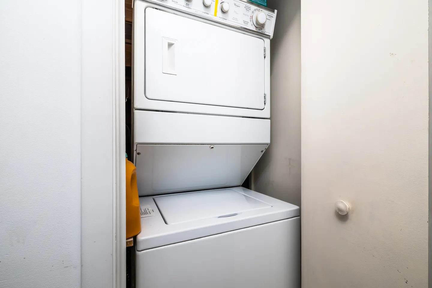 A stacked white washer and dryer unit inside a narrow utility closet.