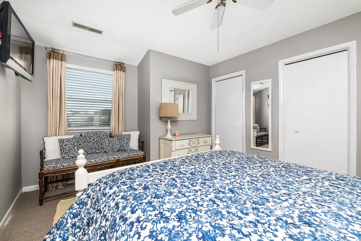 Bedroom featuring a bed with a blue and white patterned bedspread, a cushioned bench by the window, and a white dresser.