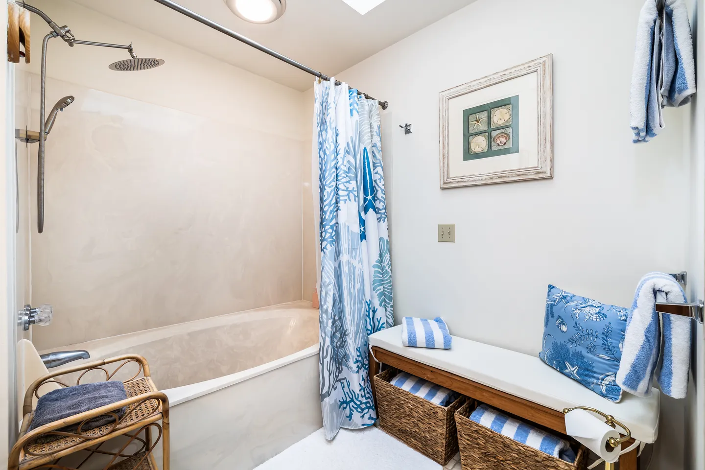 Bathroom with a bathtub and shower combination, coastal shower curtain, and a padded bench holding towels and baskets.