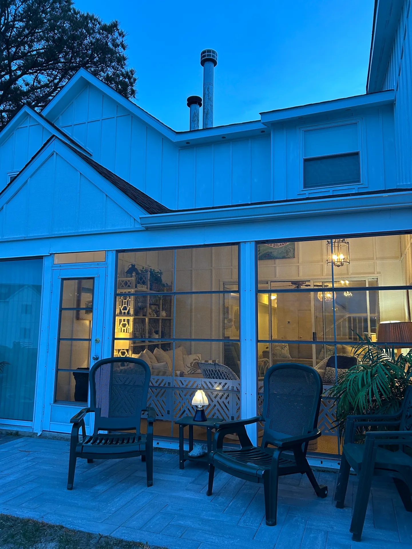 Exterior patio with outdoor chairs at dusk in front of a screened porch illuminated by warm interior lighting.