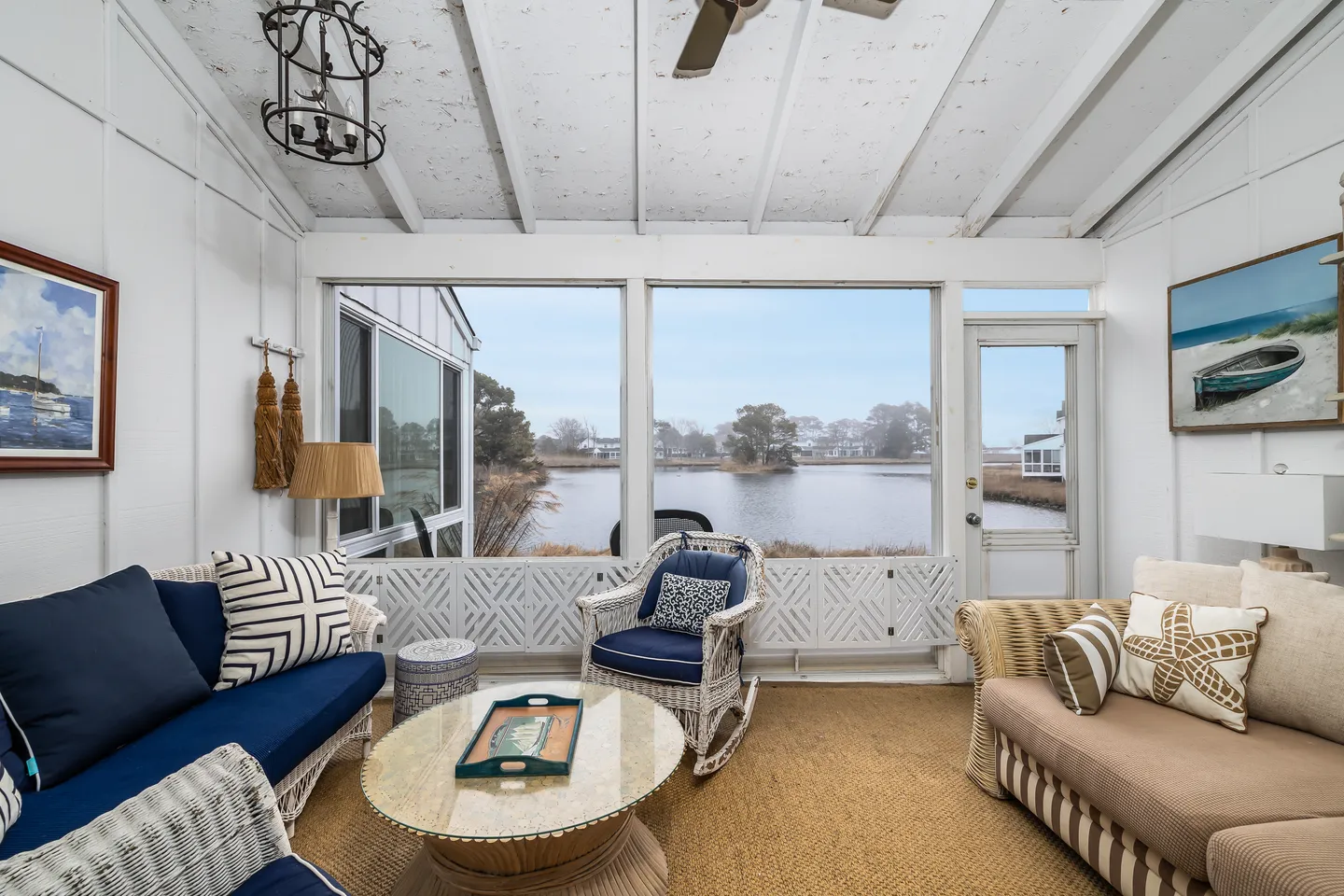 Screened porch furnished with wicker seating, a coffee table, and an exterior door overlooking a calm body of water.