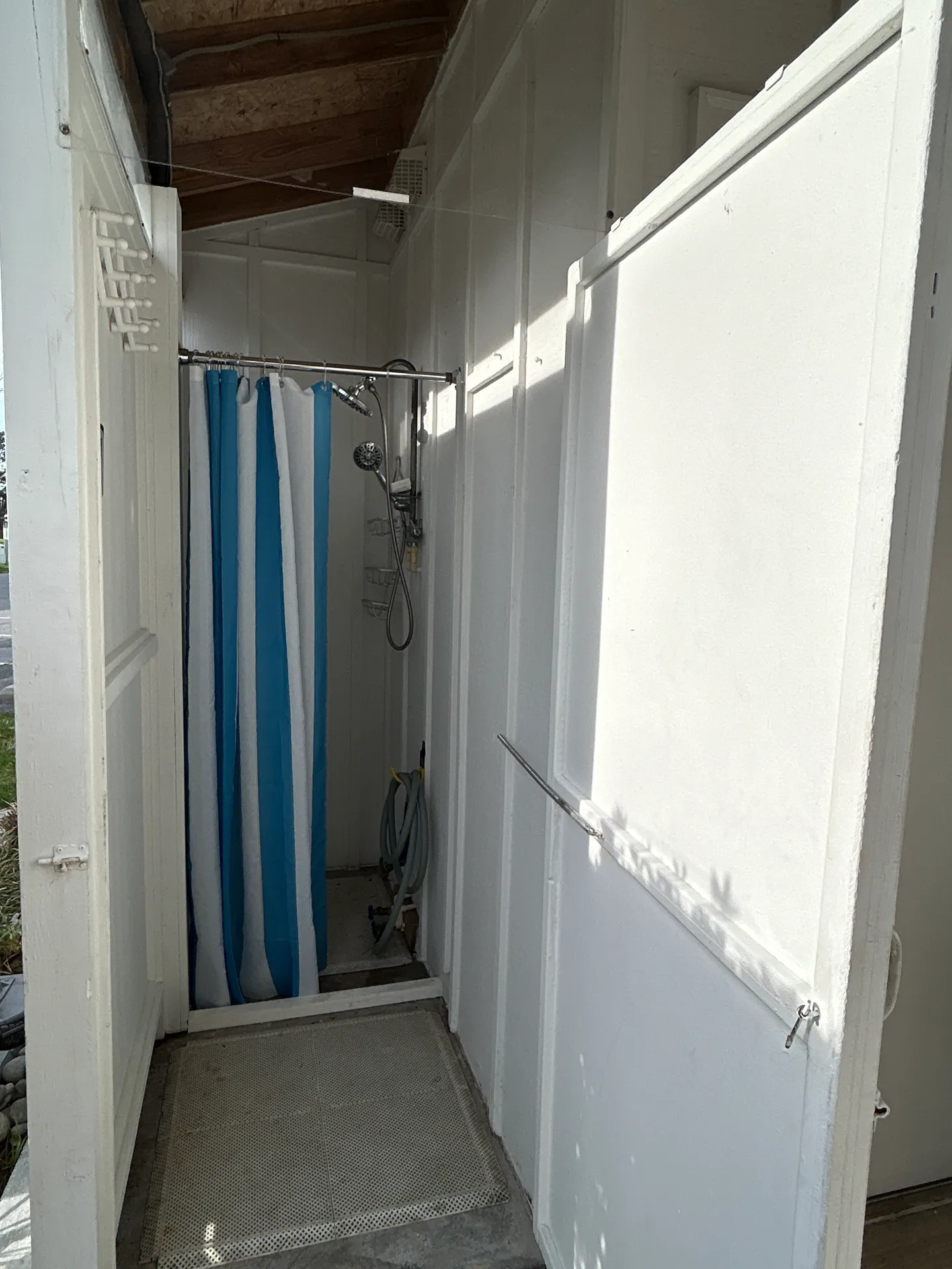 Outdoor shower enclosure with white paneled walls, a blue and white striped curtain, and a silver showerhead.