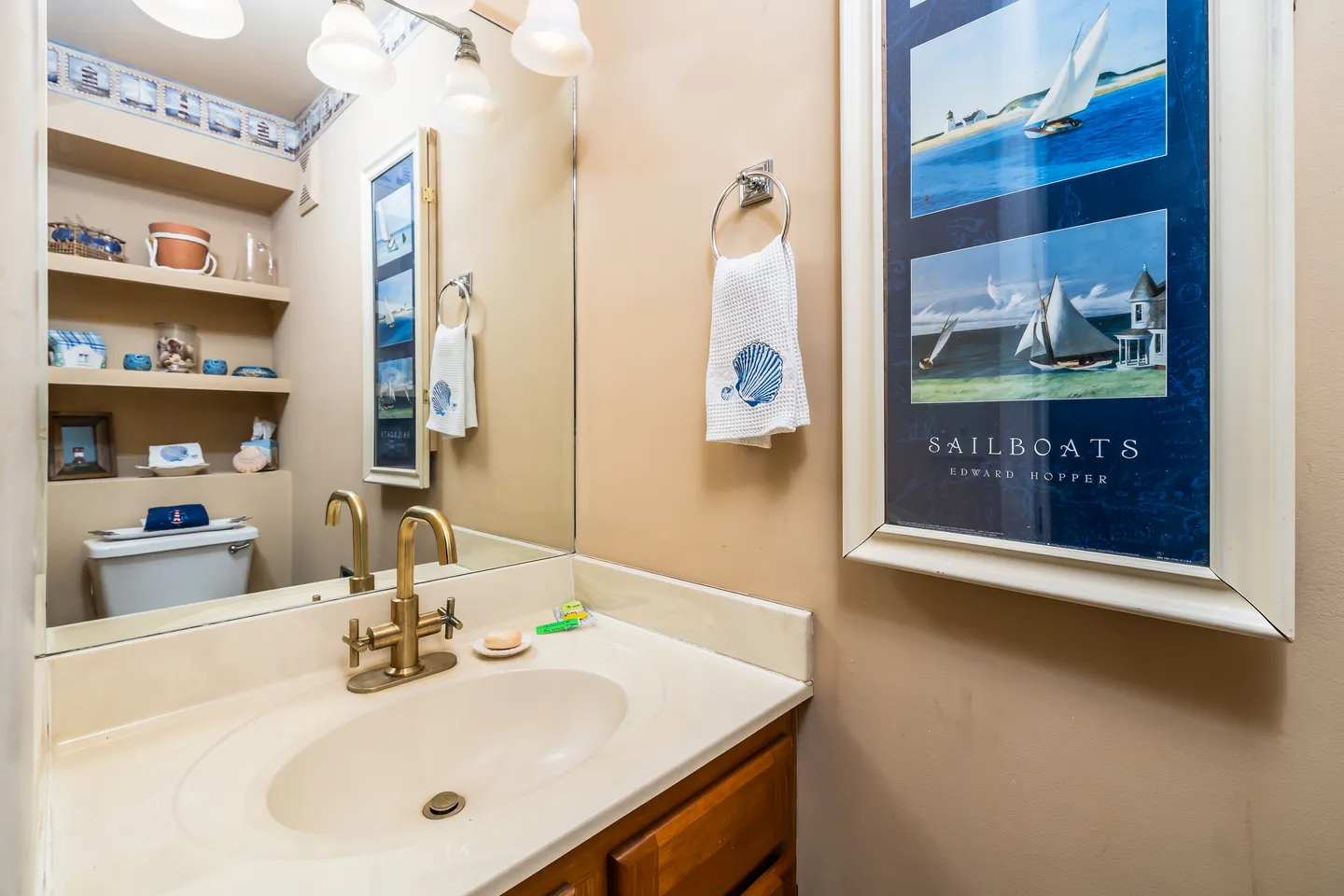 Bathroom vanity with brass faucet, large mirror, and framed sailboat art on the wall.