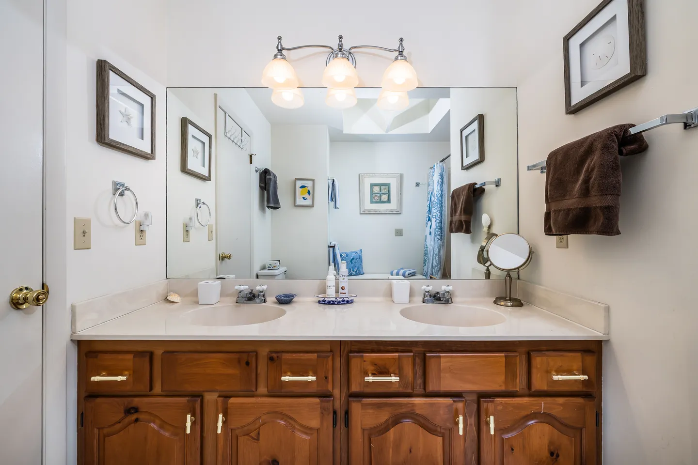 Bathroom with a double sink vanity, large wall mirror, overhead lighting fixture, and a reflection of the toilet and shower area.