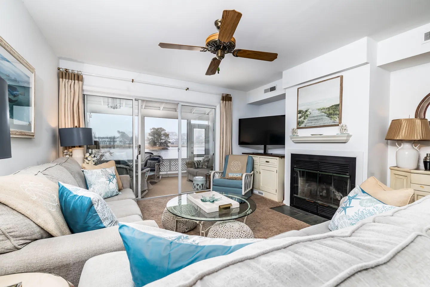 Living room with sectional sofa, glass coffee table, fireplace, television, and sliding glass doors leading to an enclosed porch with water views.