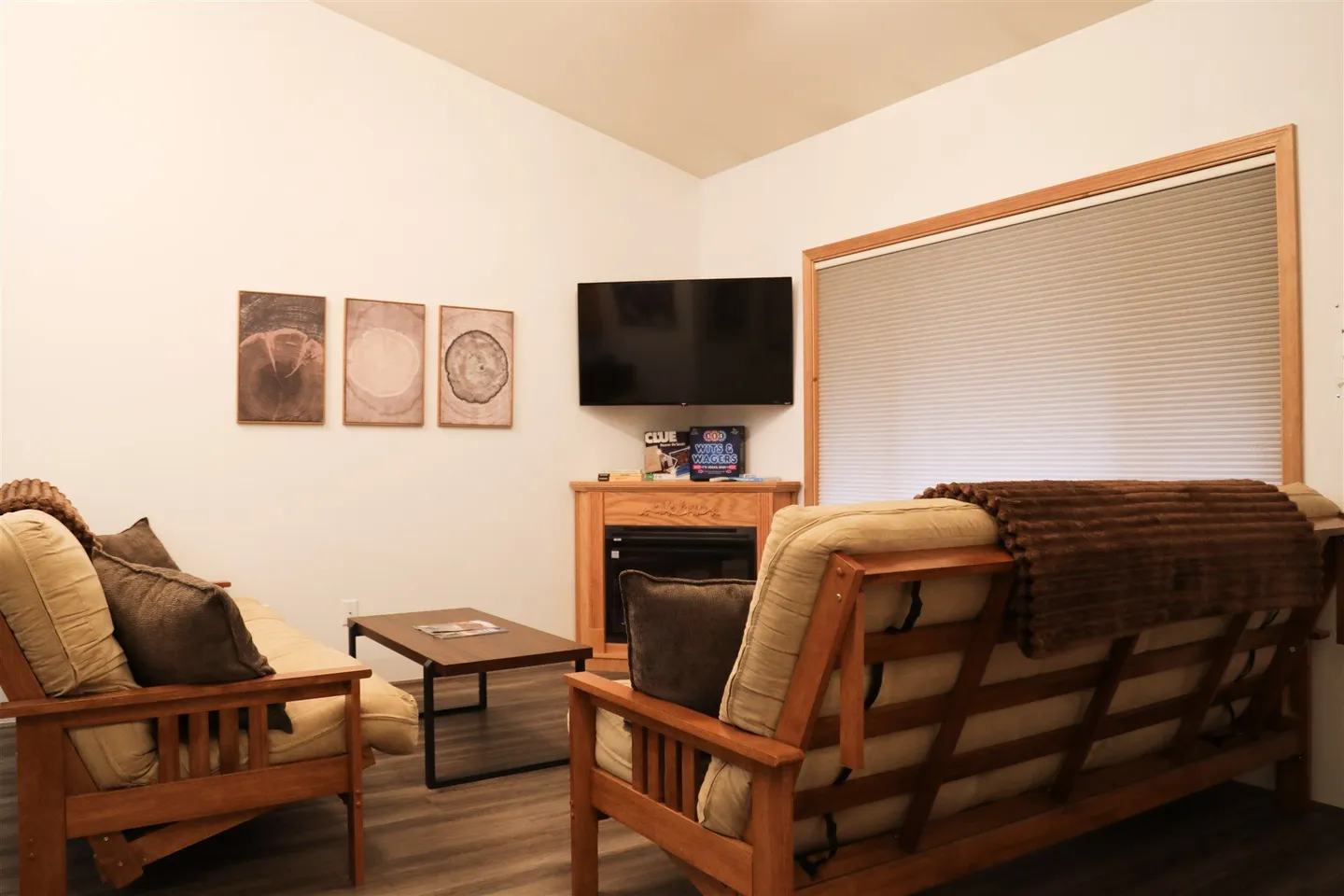 Living area with two wooden-frame futon sofas facing a corner fireplace and a wall-mounted TV.