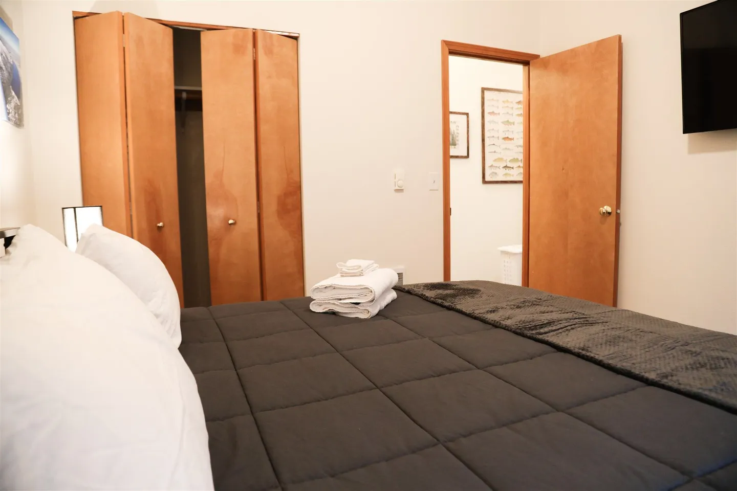 Bedroom with a bed made with a dark comforter and folded white towels, viewed toward a closet and an open doorway.