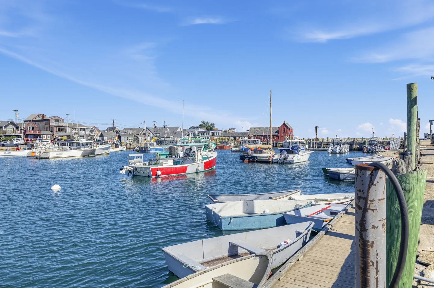 Harbor view with small skiffs tied along a wooden pier and boats anchored in the water under a clear blue sky.