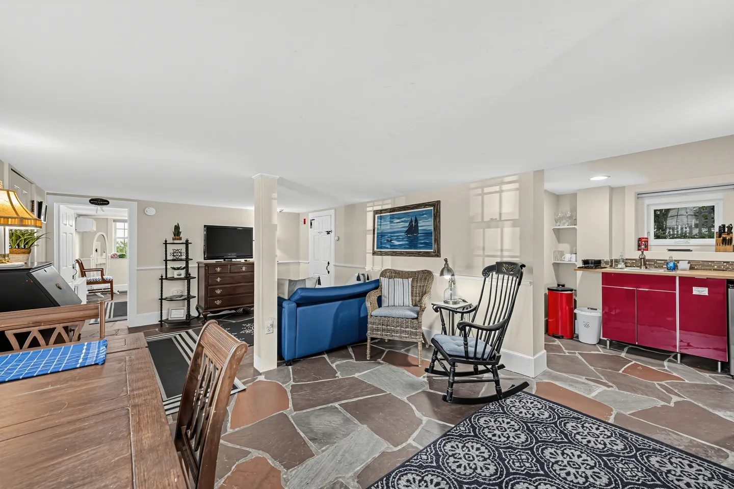 Living and dining space with stone tile flooring, low white ceiling, seating area, and kitchenette corner.