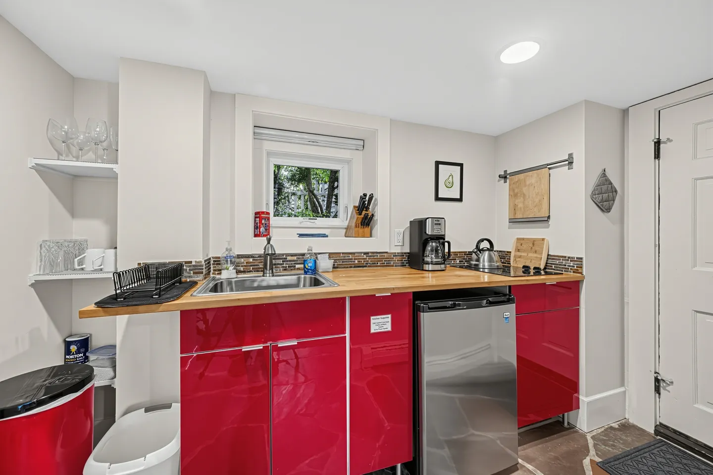Compact kitchenette with glossy red cabinets, light wood countertop, sink, mini fridge, and coffee maker.