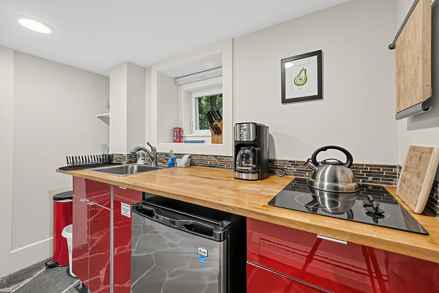 Compact kitchenette with glossy red cabinets, light wood countertop, electric stovetop, coffee maker, and mini fridge.