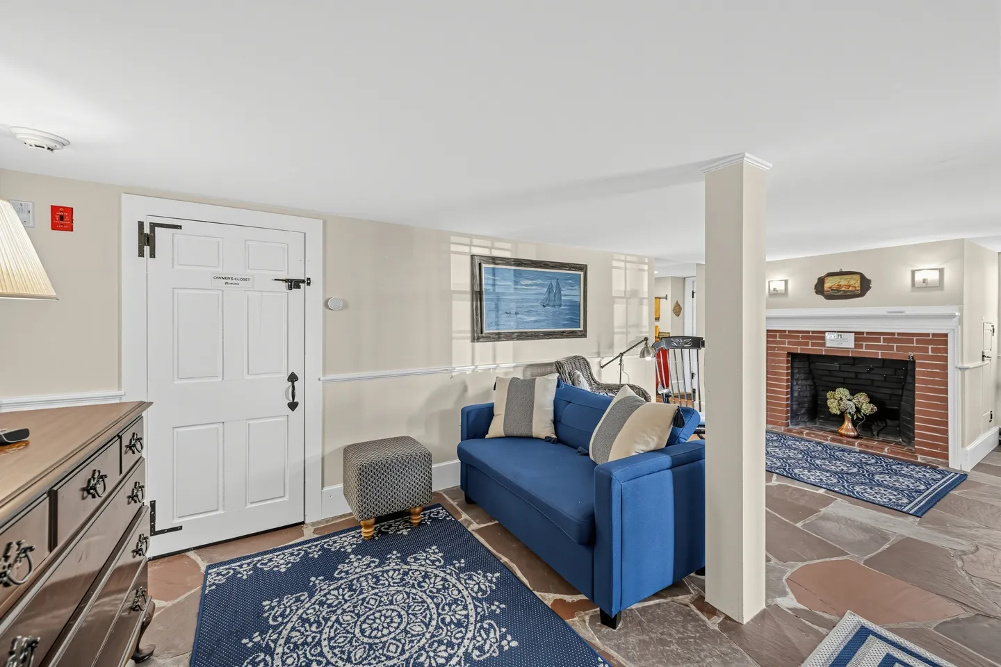 Living area with stone flagstone floors, a bright blue loveseat, patterned area rugs, and a brick fireplace.