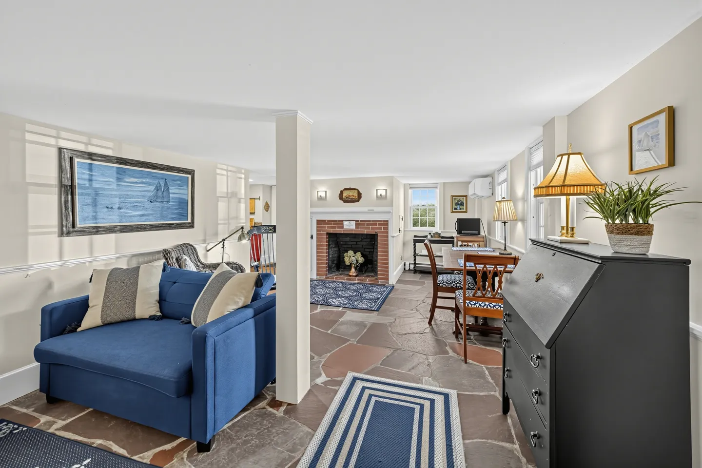 Living area with stone flagstone floors, a blue armchair, a dining nook, and a brick fireplace.