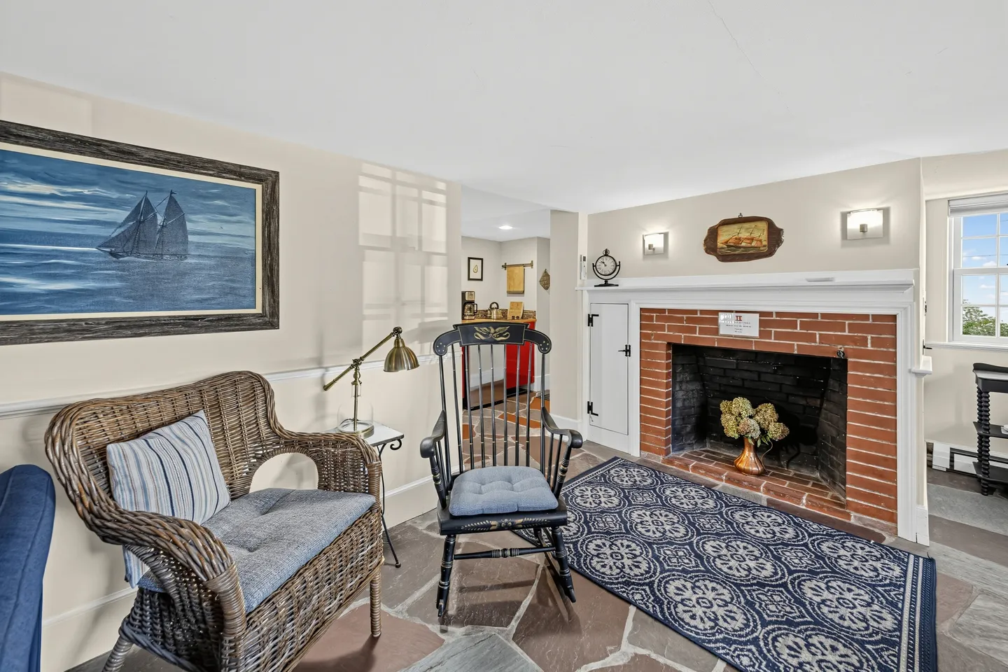 Living room featuring a brick fireplace, stone flagstone flooring, a wicker armchair, and a black rocking chair.