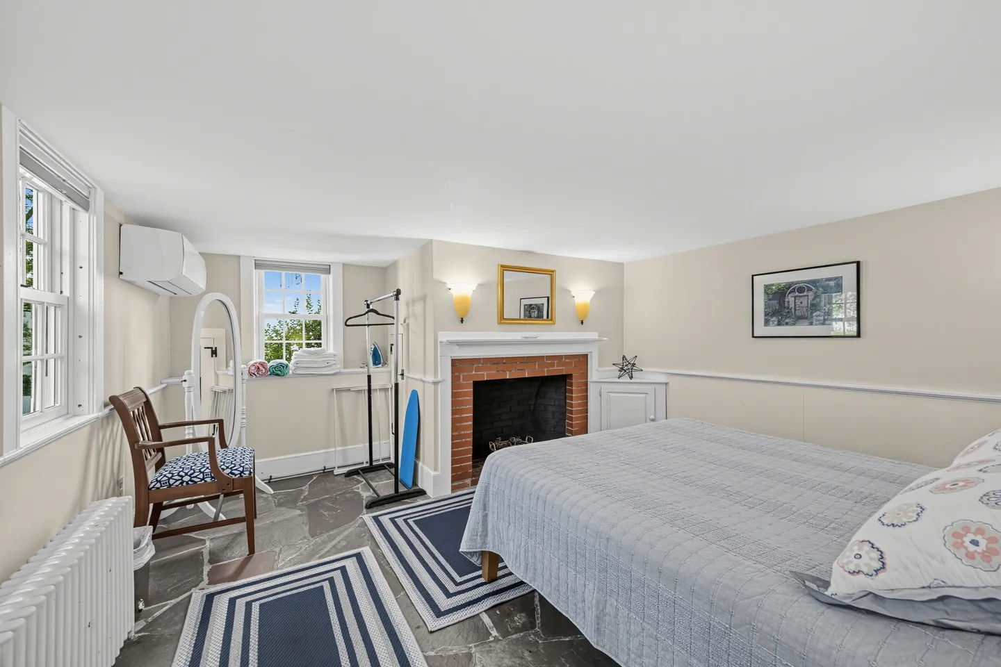 Bedroom with stone-look tile flooring, a brick decorative fireplace, and a bed made with blue bedding.