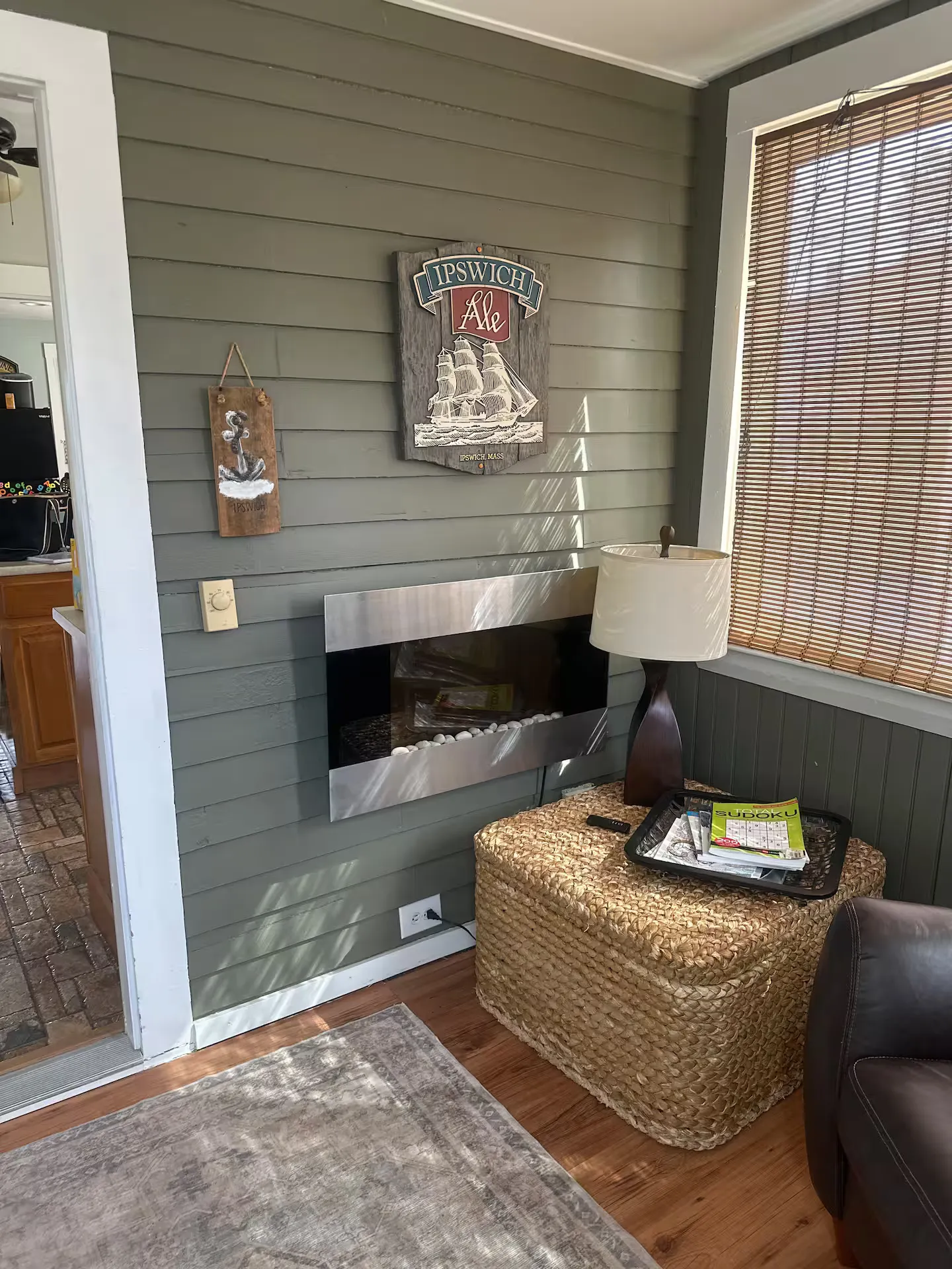 Enclosed porch or sunroom corner featuring an electric wall fireplace, woven storage chest, table lamp, and nautical wall decor.