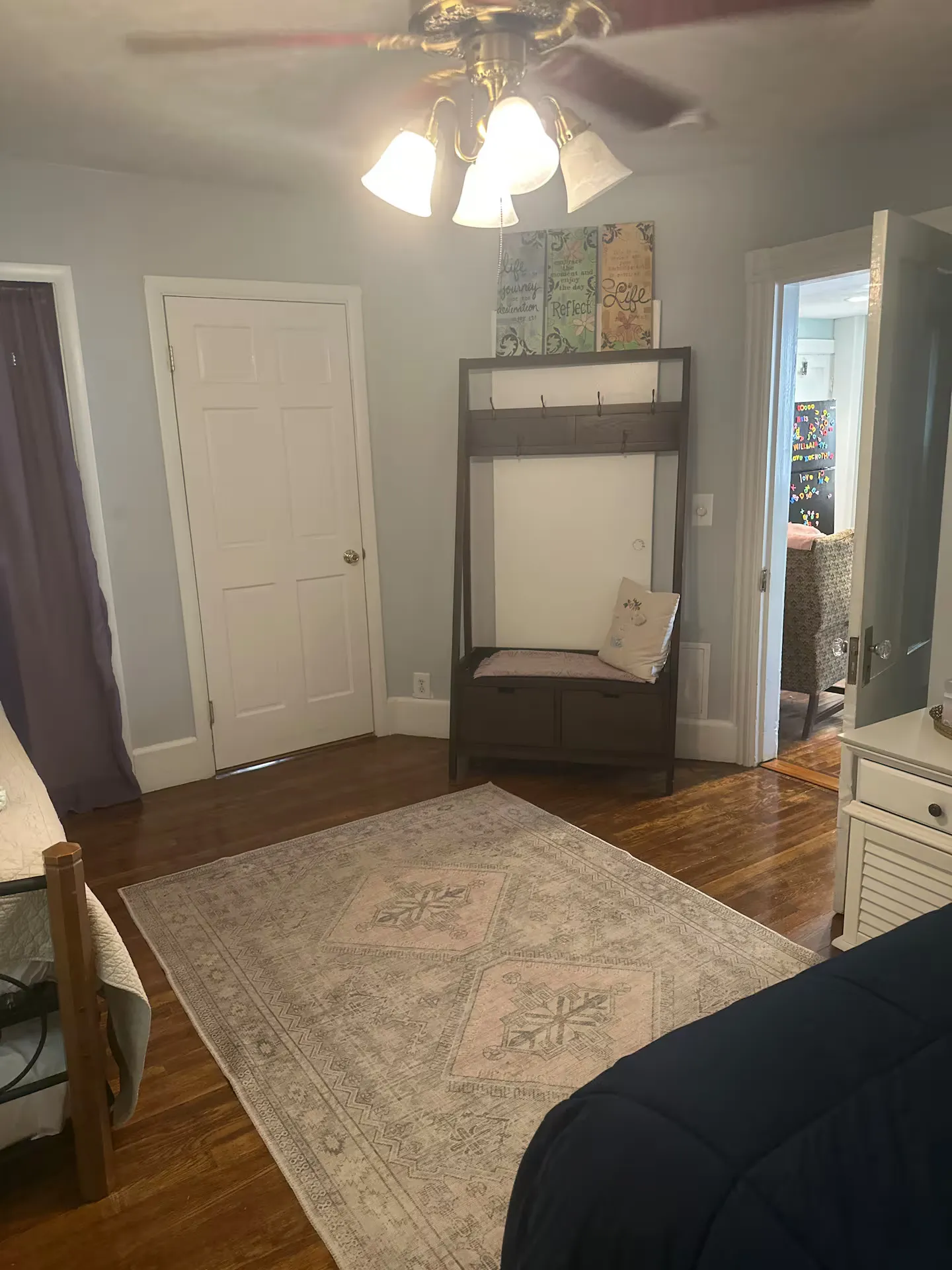 Bedroom with hardwood floors, a patterned area rug, a ceiling fan, a coat rack bench, and an open doorway leading to another room.