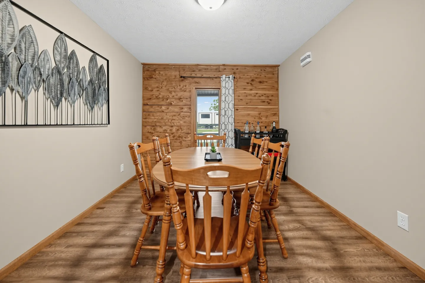 Dining area with a wooden oval table and chairs, wood-look flooring, a wood-paneled accent wall, and a door leading outside.