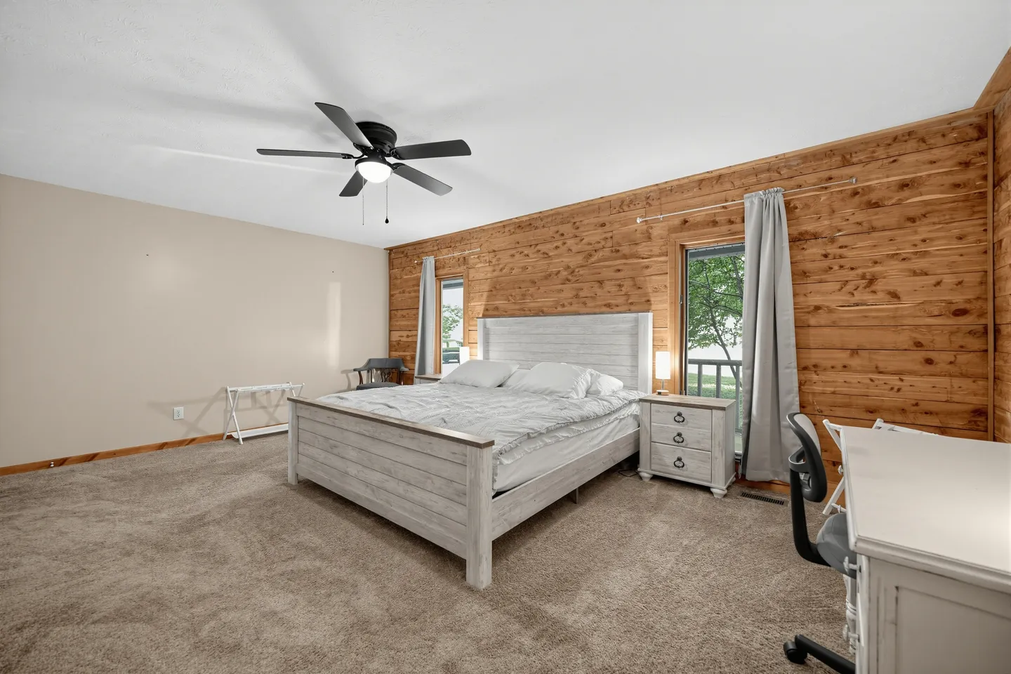 Bedroom featuring a wood-paneled accent wall, a light-colored wooden bed, a nightstand, and a desk with an office chair.