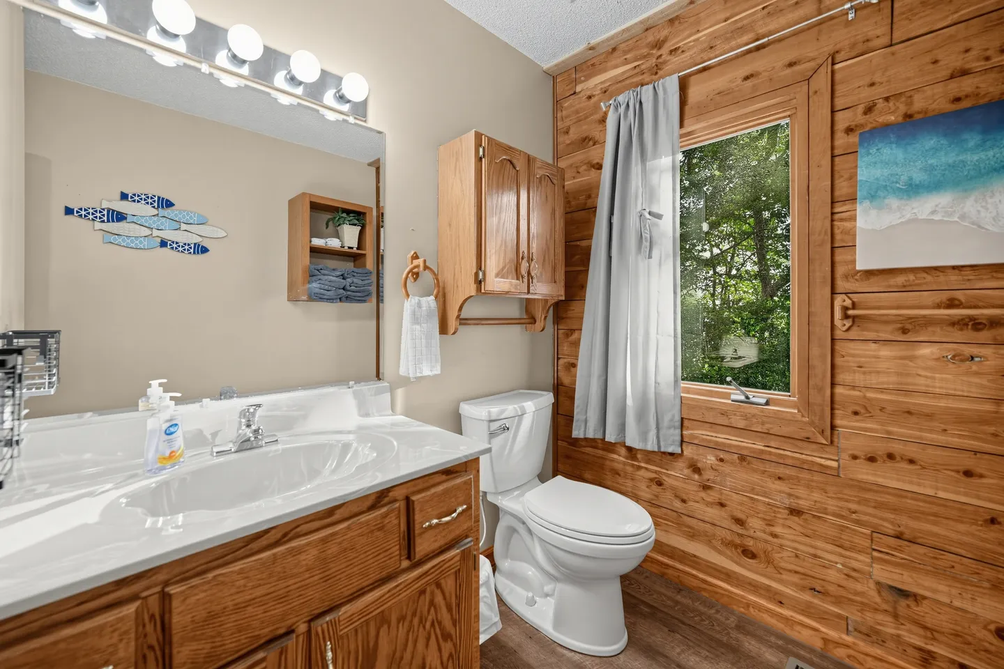 Bathroom with a wood-grain vanity, toilet, and wood-paneled accent wall with a window.