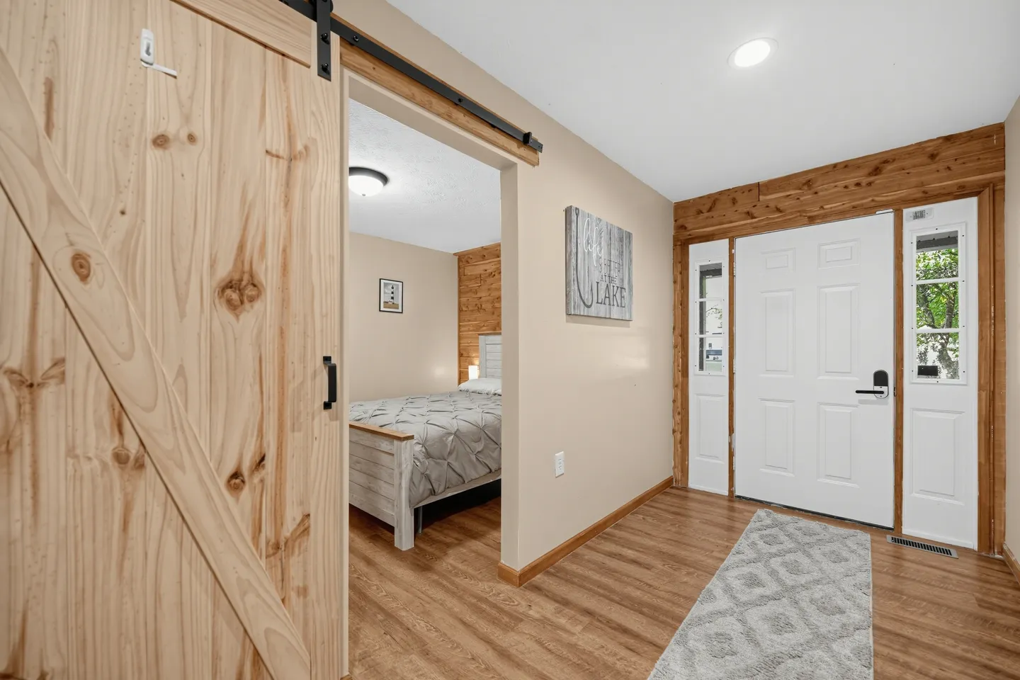 Entryway with a white front door and sidelight windows next to a sliding wooden barn door leading into a bedroom.