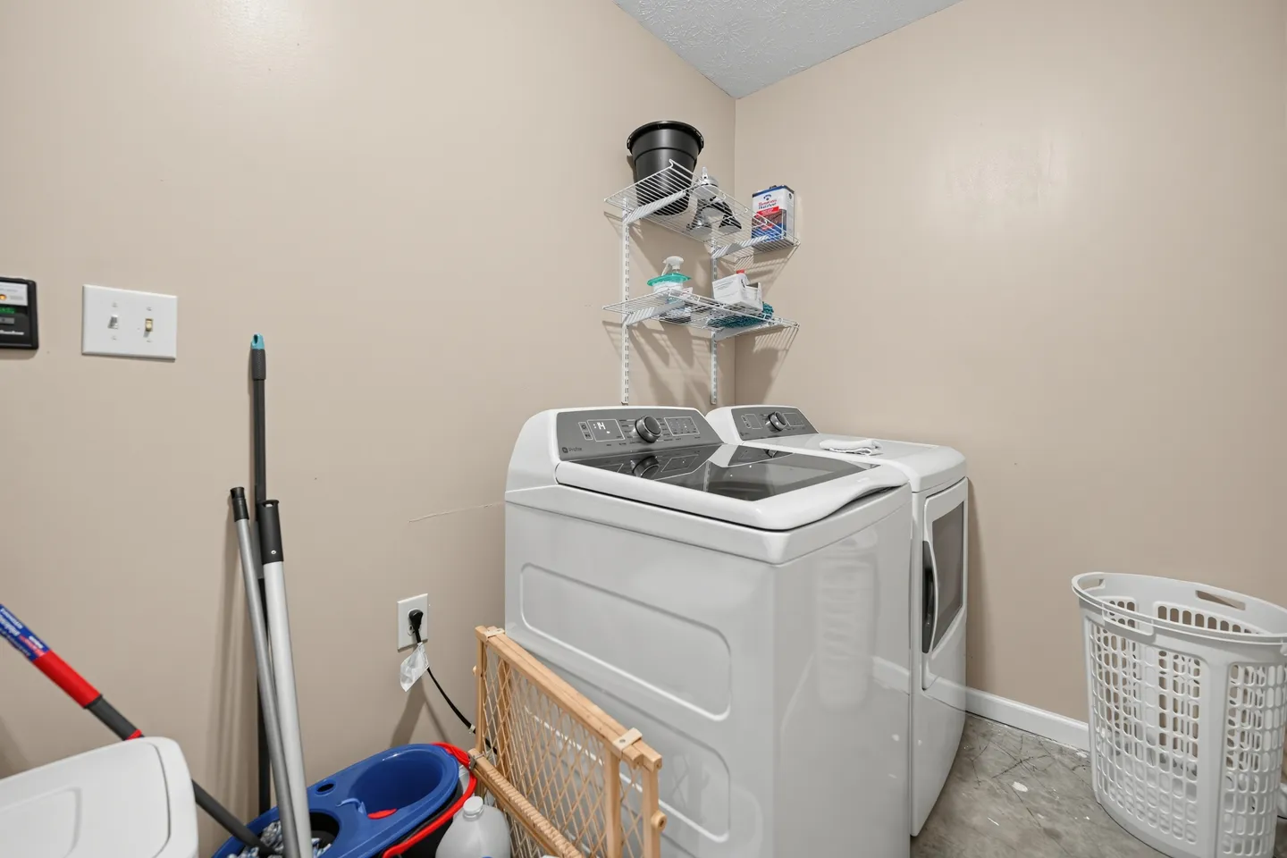 Laundry room with a white washing machine, dryer, wire wall shelving, and cleaning supplies.
