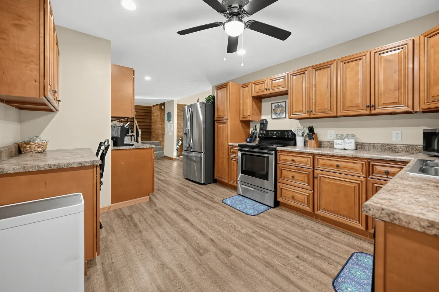 Kitchen with wood cabinetry, stainless steel appliances, laminate counters, and wood-look flooring under a ceiling fan.