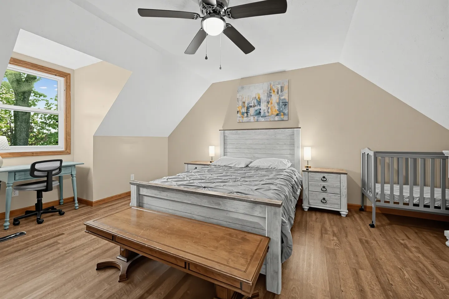 Bedroom with angled ceilings, a rustic wooden bed, matching nightstands, a crib, and a desk under a window.
