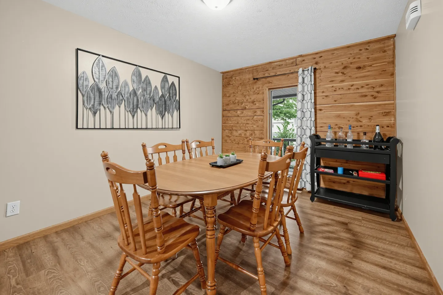 Dining room with a wooden table, matching chairs, a wood-paneled accent wall, and a black bar cart.