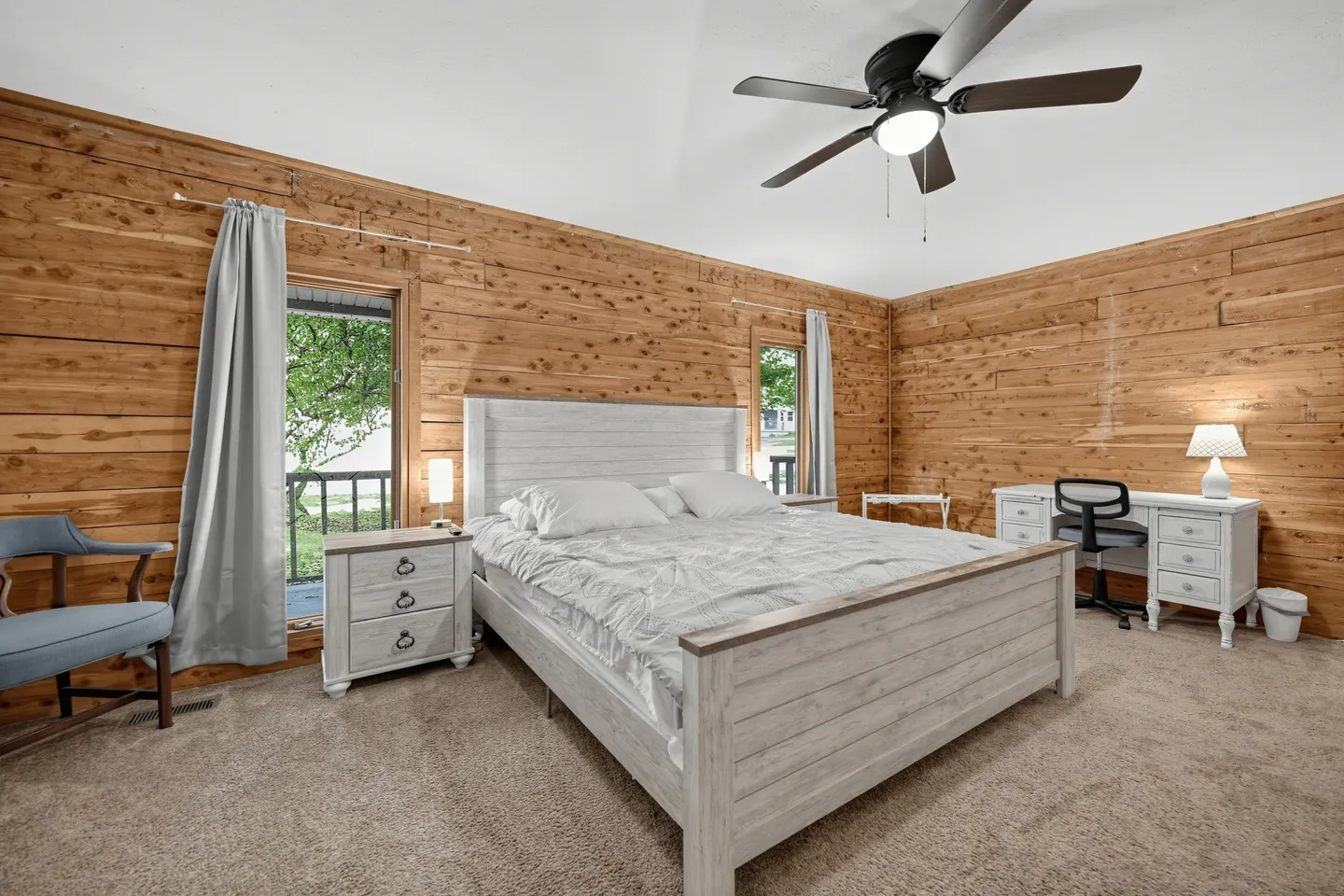 Bedroom with log-paneled walls, carpeted flooring, a light wood bed frame, nightstand, and a desk with a chair.