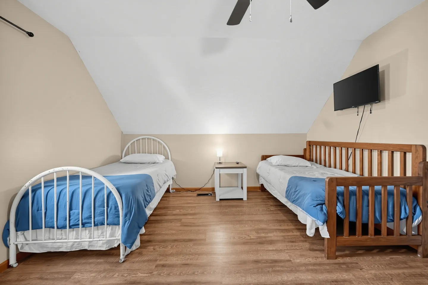 Attic bedroom with sloped ceilings, two twin beds, wood-look flooring, and a wall-mounted TV.